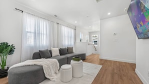 A modern living room with a grey sofa, a white rug, and a potted plant. - Spacious 7-BR Home in Hayward with A/C &Parking (Hayward)