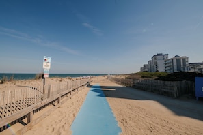 Ein Strandweg mit einer blauen Matte, Holzzaun und einem Hinweisschild.