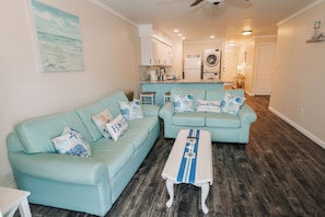 A living room with two light blue sofas, a white coffee table, and a kitchen in the background. - Family Getaway! Modern 2BR Condo + Bonus Bunk Room - Sleeps 8 (Ocean City)
