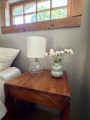 A wooden bedside table with a clear glass lamp and a vase of white flowers. - Historic Cabbagetown Loft - Walk to BeltLine, Parks, Dining & Bars (Atlanta)