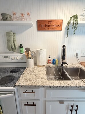 A kitchen with a granite countertop, stainless steel sink, and a wooden sign that reads 'The Bird House.' - Historic Cabbagetown Loft - Walk to BeltLine, Parks, Dining & Bars (Atlanta)