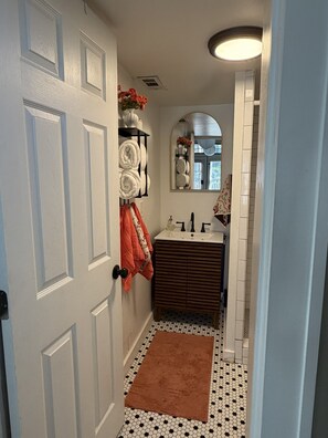 A bathroom with a white door, a towel rack with folded towels, a brown rug, a sink with a mirror above it, and a patterned floor. - Historic Cabbagetown Loft - Walk to BeltLine, Parks, Dining & Bars (Atlanta)