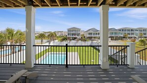 A covered deck with a view of a swimming pool and a residential area. - Ocean Views! One Row to the Beach with Pool & Spa (Oak Island)