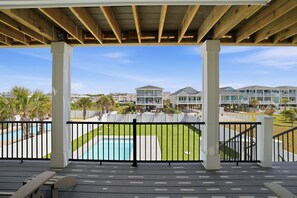 A covered deck with a view of a swimming pool and a residential area. - Ocean Views! One Row to the Beach with Pool & Spa (Oak Island)