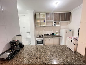 Una cocina compacta con armarios blancos, encimera de granito, estufa, lavamanos y refrigerador.