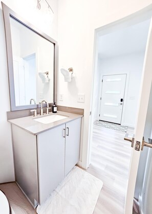 Uma casa de banho moderna com um espelho grande, duas lavatórios e uma porta que dá para outro espaço.