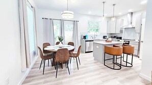Una cucina moderna con isola centrale, zona pranzo con tavolo rotondo e angolo bar con sgabelli.