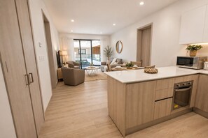 Eine moderne Küche mit Kochinsel, ein Essbereich mit rundem Tisch und ein Wohnzimmer mit Sofa und Sesseln.