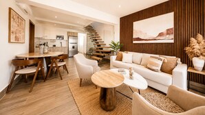 Ein modernes Wohnzimmer mit Sofa, Couchtisch und Sesseln. Eine Treppe führt zu einer oberen Ebene.