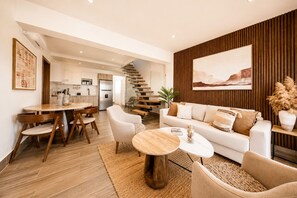 Ein modernes Wohnzimmer mit Sofa, Couchtisch und Sesseln. Eine Treppe führt zu einer oberen Ebene.