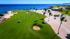 Ein Golfplatz mit Blick auf den Ozean, Sandbunkern und Palmen.