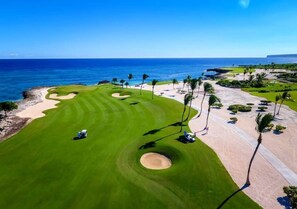 Ein Golfplatz mit Blick auf den Ozean, Sandbunkern und Palmen.