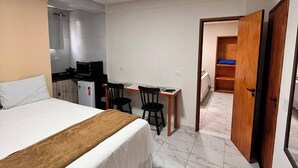 A hotel room with a bed, a desk, and a chair. There is a door leading to another room. - Porto Beach Flats (Ipojuca)