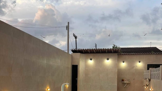 A swimming pool with lounge chairs and a table, surrounded by a low wall and a building with a tiled roof. - Porto Beach Flats (Ipojuca)