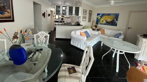 A modern living room with a dining area, white furniture, a kitchen in the background, and a ceiling fan.