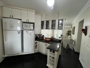 A kitchen with white cabinets, a black countertop, a microwave, and a refrigerator. - Ocean view, 3 bedrooms, beach service and close to everything in Riviera. (Bertioga)