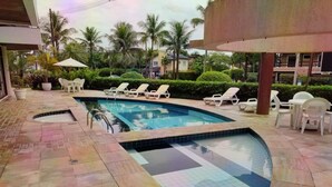 A swimming pool with lounge chairs and umbrellas, surrounded by palm trees and a tiled patio.