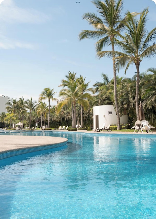 A swimming pool with clear blue water, surrounded by palm trees and lounge chairs.