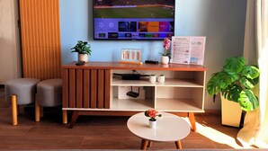 A modern hotel room with a wooden TV stand, a flat-screen TV displaying a sports channel, a small table with a potted plant, and a large window with curtains. - Downtown Rio • VLT at the Door • Pool • Wi-Fi • 20 min Copacabana. (Rio de Janeiro)