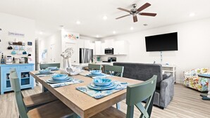 Eine moderne Küche mit weißen Schränken, einem Holzespeisetisch gedeckt mit blauen Tellern und einem grauen Sofa im Wohnbereich.