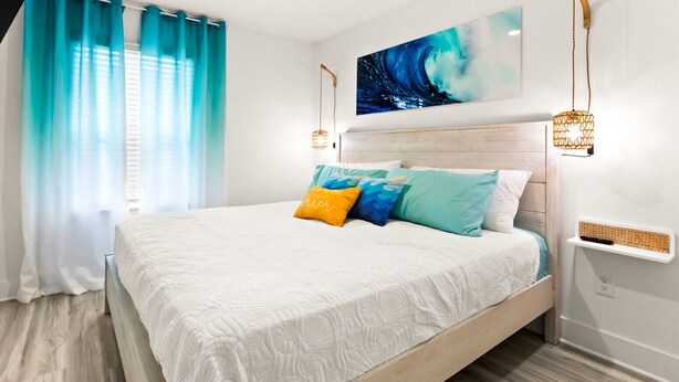 Ein Schlafzimmer mit Bett, Vorhängen, einem Wandbild und Nachttischlampen.