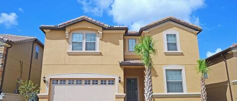 A two-story house with a garage, a front door, and a small garden with a palm tree.