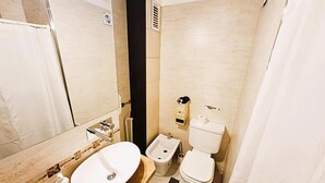 Un baño con tocador de madera, lavamanos, inodoro y cortina de ducha.