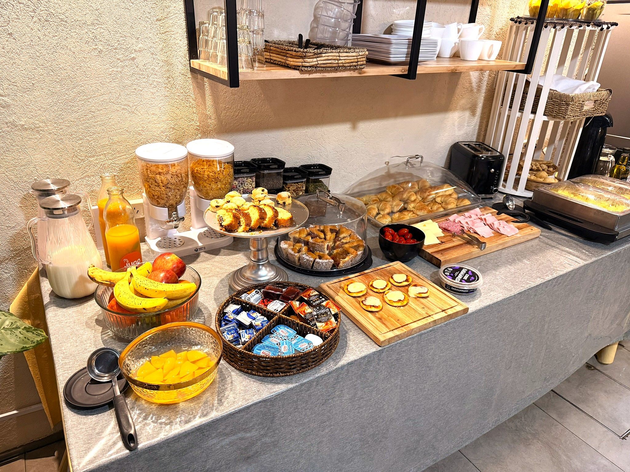 A buffet with various food items and beverages, including fruits, pastries, and condiments.