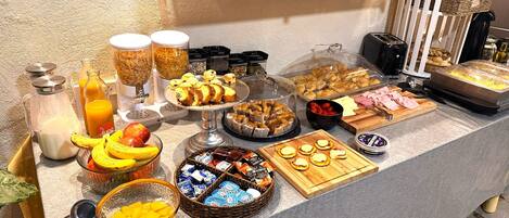 A buffet with various food items and beverages, including fruits, pastries, and condiments.
