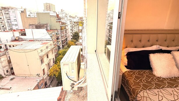 Un dormitorio con cama, ventana y vistas a un paisaje urbano.