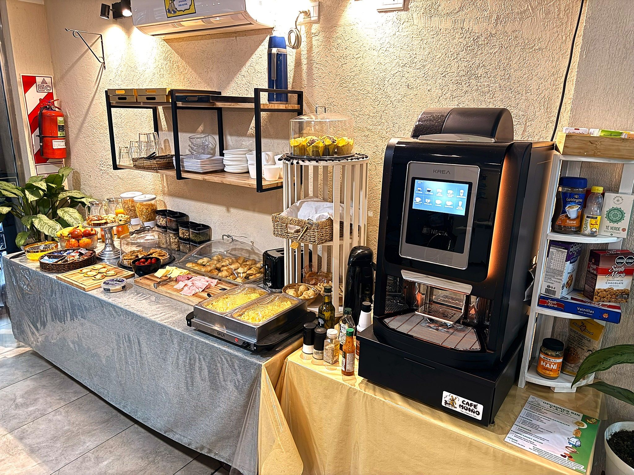 Montaje de bufé con distintos alimentos, una máquina de café y un extintor.
