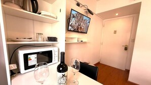 Cocina compacta con microondas, una botella de vino y vasos sobre la encimera, un televisor en la pared y una puerta con un cartel de prohibido fumar.