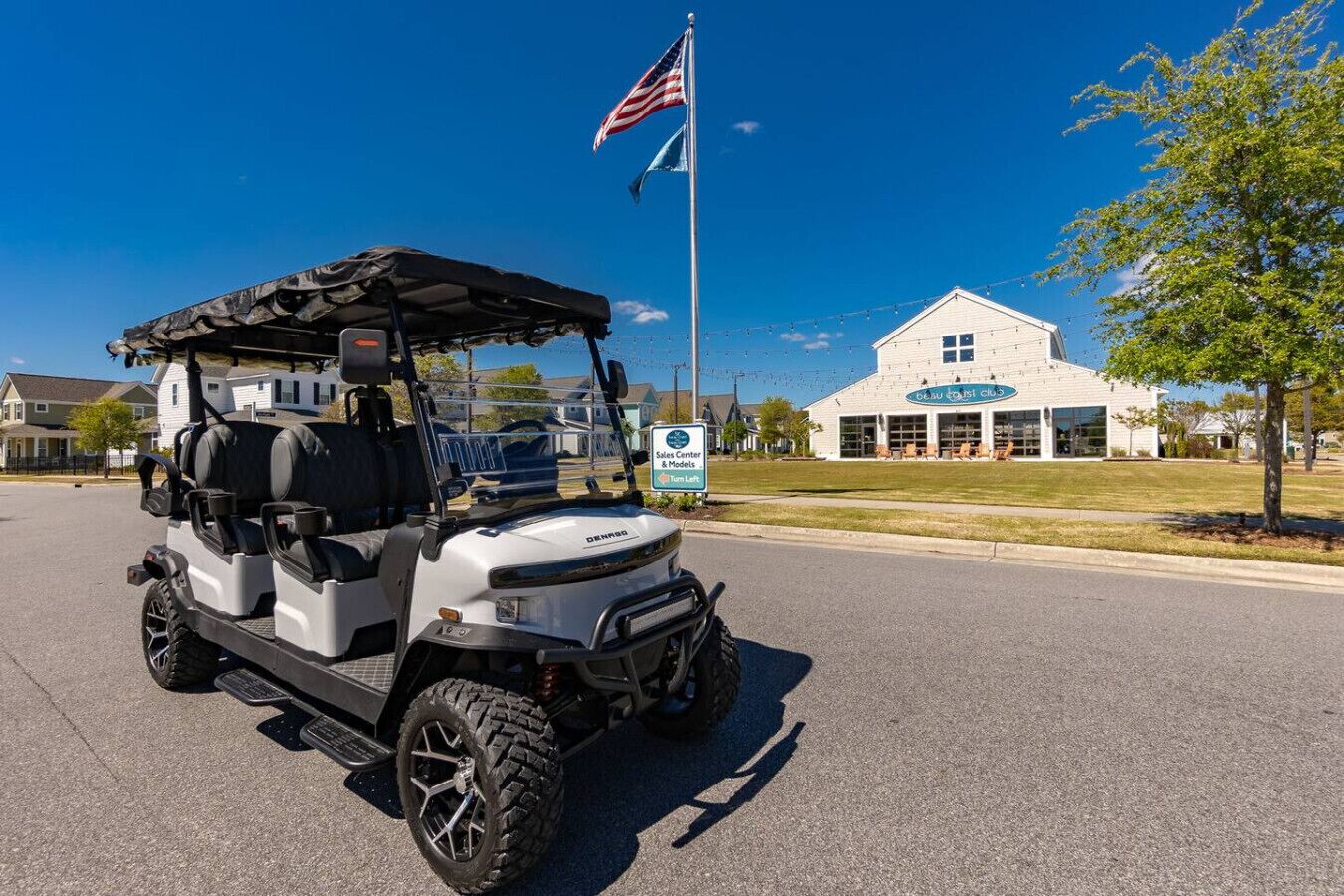 A golf cart parked on a street with a building labeled 'Sales Center & Models' in the background.