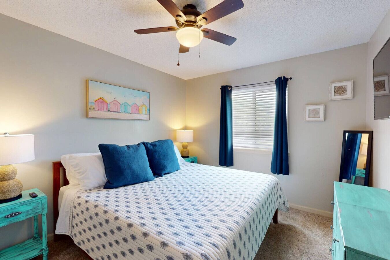 A bedroom with a bed, two bedside tables, a ceiling fan, a window with curtains, and a wall-mounted painting.