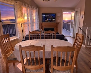 Ein Wohnzimmer mit Kamin, Fernseher und einem Balkon mit Sonnenuntergangsblick.