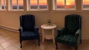 A room with two chairs, a small table, and a view of a sunset through large windows.