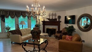 Uma sala de estar com um candelabro, lareira, sofá, mesa de centro e um espelho grande.
