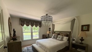 Quarto com cama grande, lustre, vista para o exterior e estátua em uma cômoda.