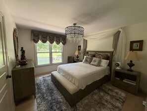 A bedroom with a large bed, a chandelier, a view of the outdoors, and a statue on a dresser.