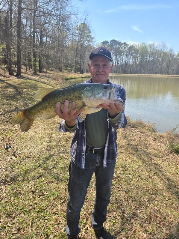 A person holding a large fish by a lake with trees in the background.