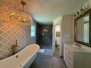 A modern bathroom with a freestanding bathtub, a large mirror, and a patterned wall.