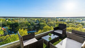 Un balcon agrémenté de meubles en osier et d’une table en verre, offrant une vue sur un paysage verdoyant luxuriant.