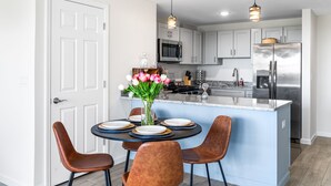 Une cuisine moderne avec des meubles blancs, un îlot central, des appareils en acier inoxydable et des luminaires suspendus.