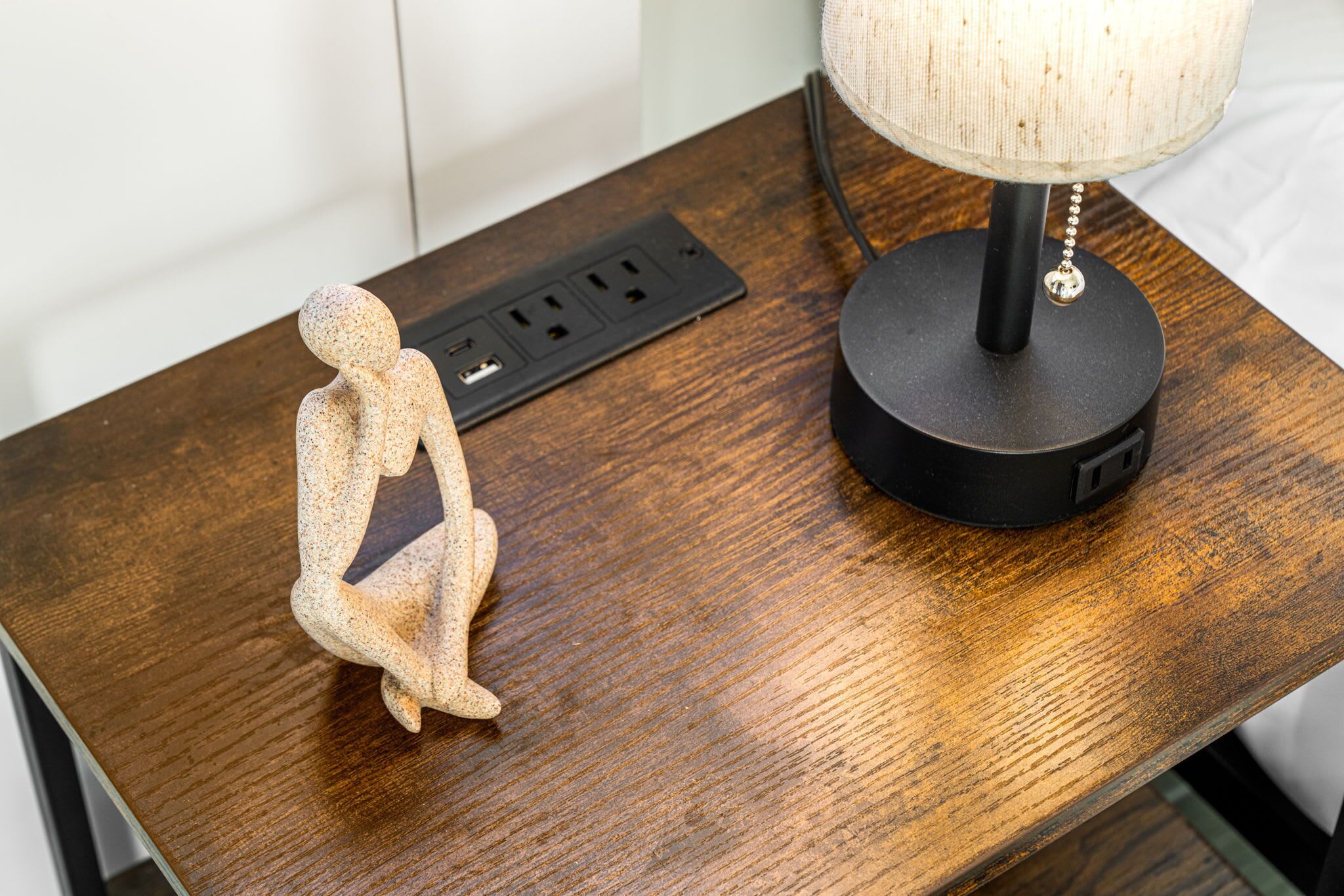 A wooden table with a power strip, a lamp, and a small figurine.