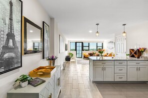 Uma cozinha moderna com ilha central, iluminação pendente e vista para uma sala de estar.