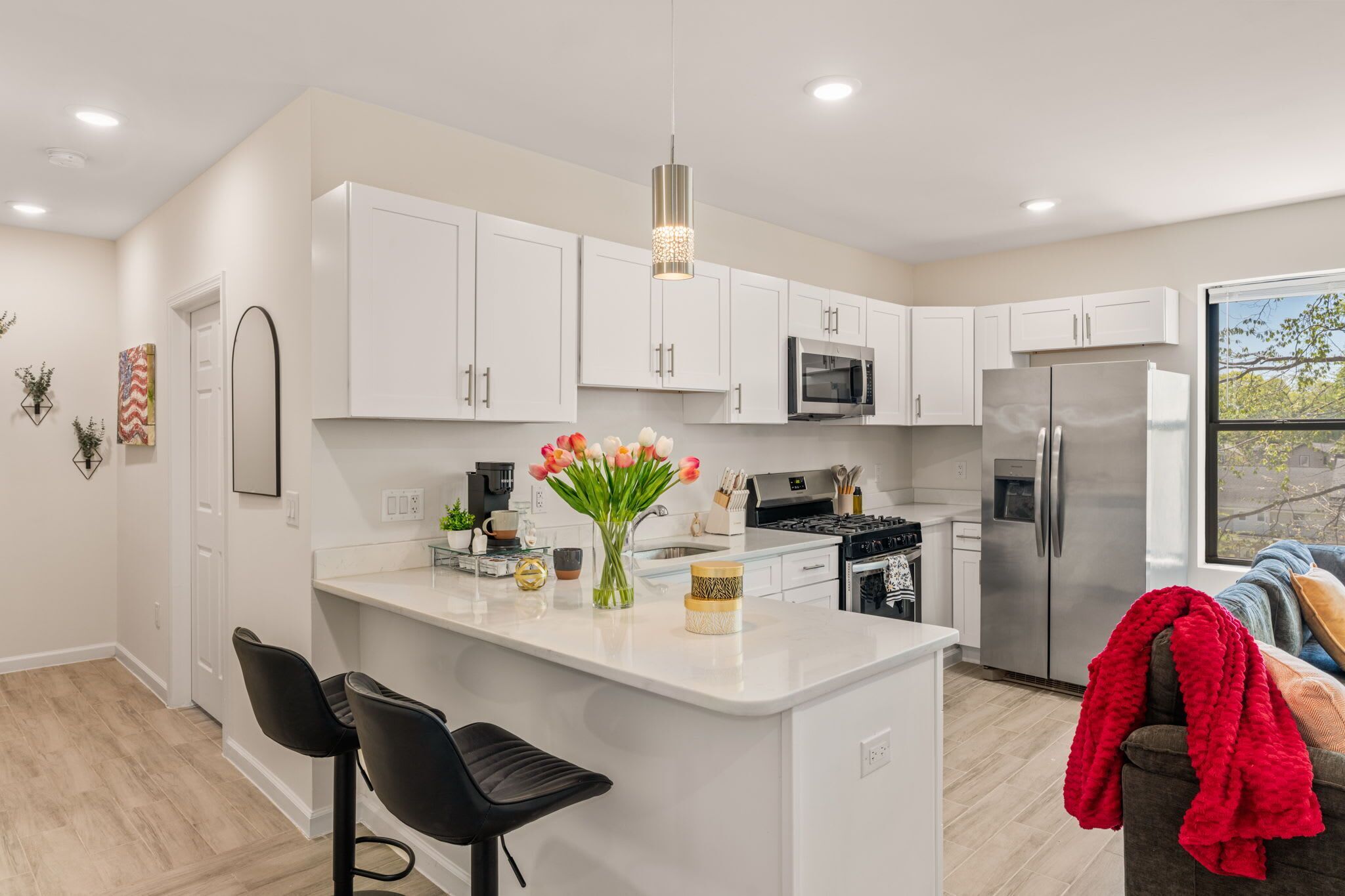 Una cocina moderna con armarios blancos, una isla central con taburetes, un refrigerador de acero inoxidable y una ventana con vistas.