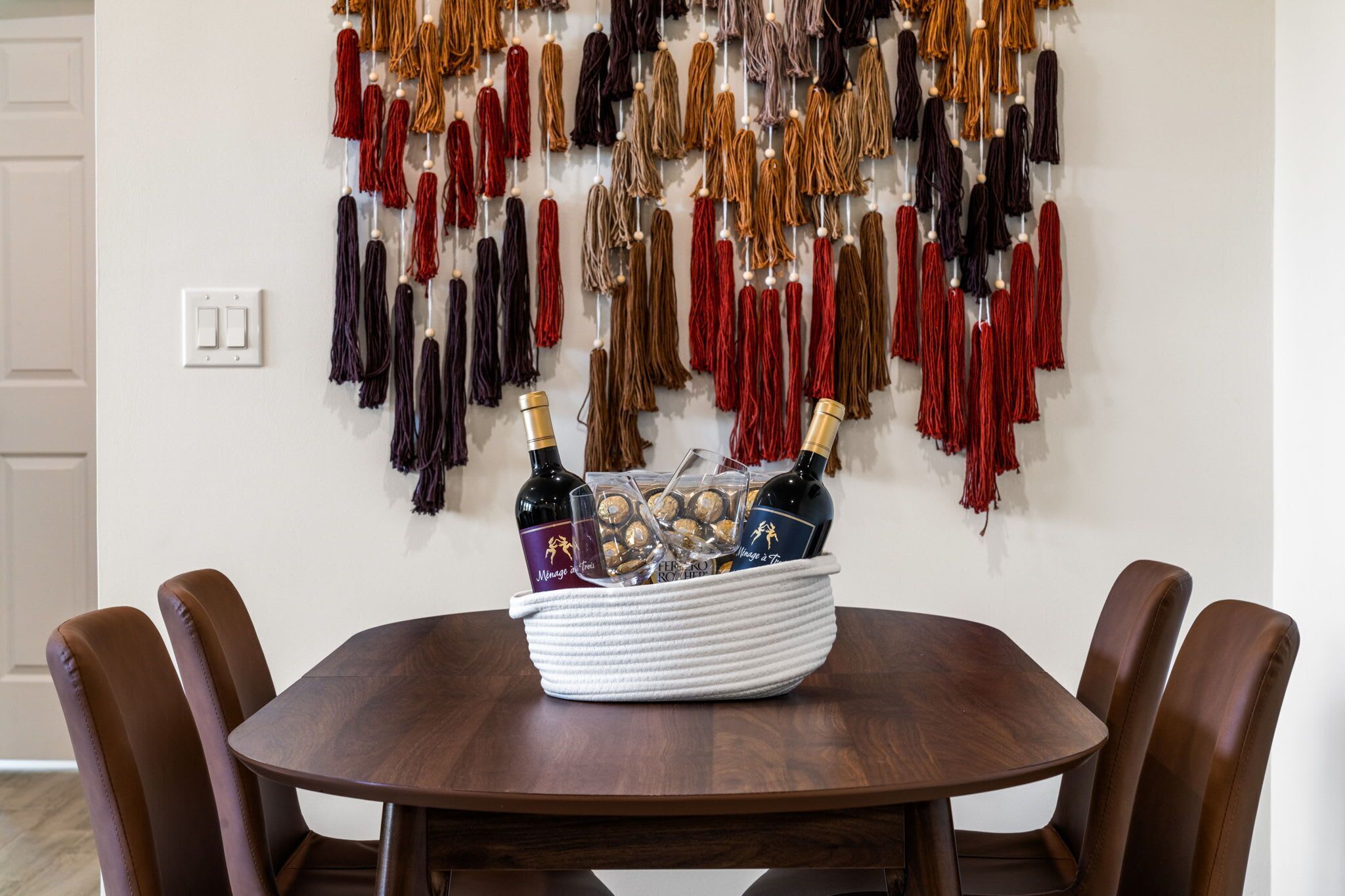 Una mesa de comedor con un cesto de botellas y copas, rodeada de sillas.
