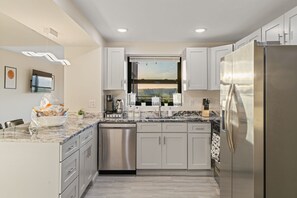 A modern kitchen with a dishwasher, stainless steel appliances, a window with a city view, and a marble countertop. - 3BR Penthouse w Hot Tub, Free Parking (East Orange)