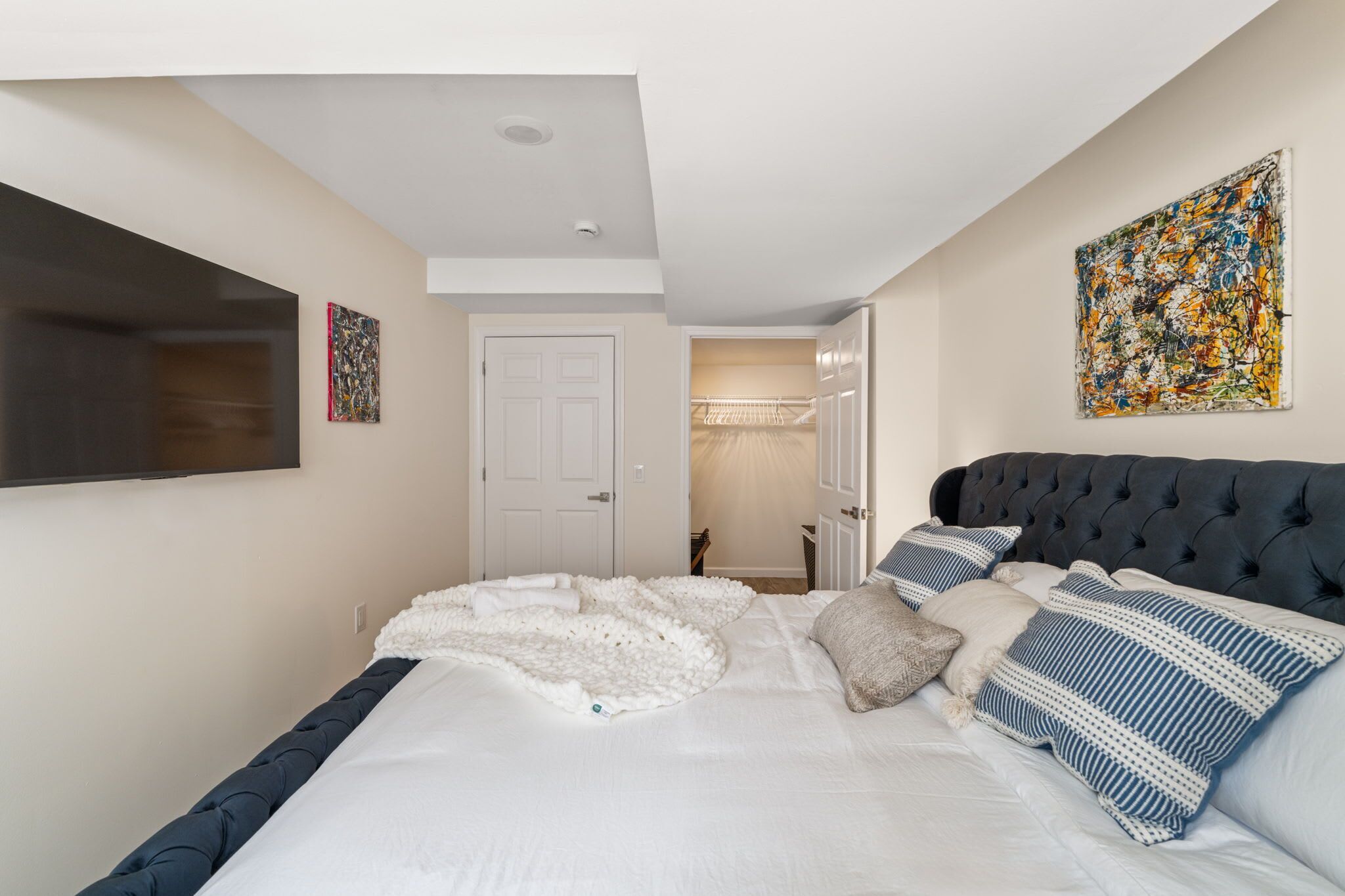 A bedroom with a bed, a large painting, a door, and a ceiling light.