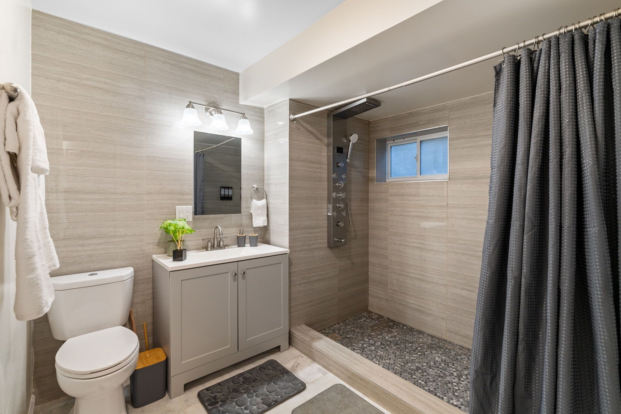 A modern bathroom with a toilet, sink, shower, and a window.